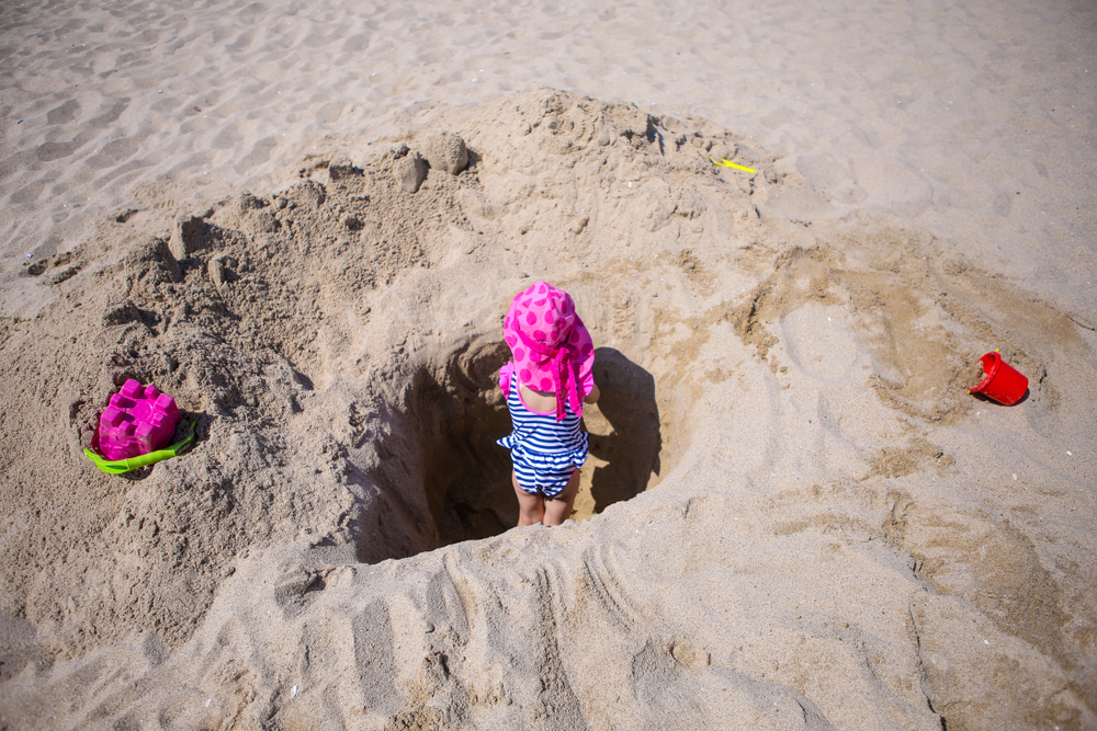 לא רק הים עלול להיות מסוכן, אלא גם החול עצמו. בכל שנה נהרגים כמה אנשים מקריסת חולות. פעוטה משחקת בבור על שפת הים | צילום: Mircea Moira, Shutterstock