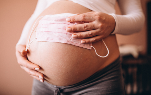 A pregnant woman holding a mask | Photography: PH888, Shutterstock